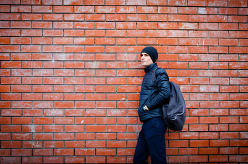a young man stands leaning against a brick wall waiting for something