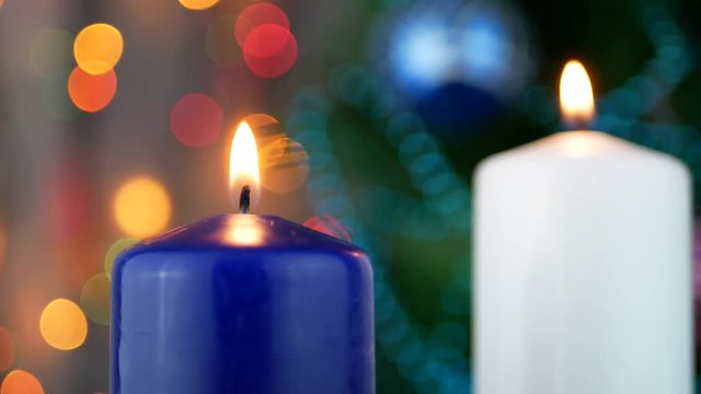 White and blue candles are burning over holiday bokeh blinking background and Christmas tree
