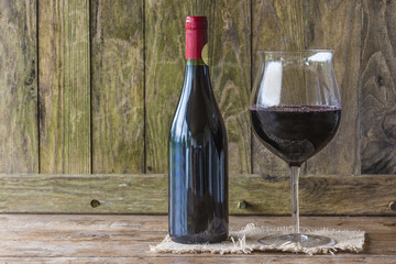 Bottle and glass of red wine on rustic background with copy space