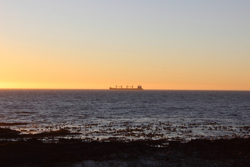 Ship in the water with orange sunset over the horizon