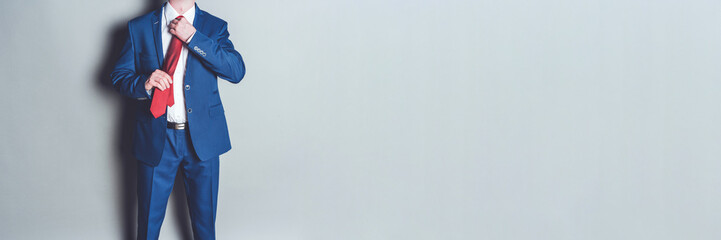 Portrait of successful businessman wearing blue suit and red tie against grey background with copy space