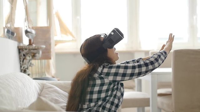 Young woman with virtual reality headset or 3d glasses sitting on sofa at home