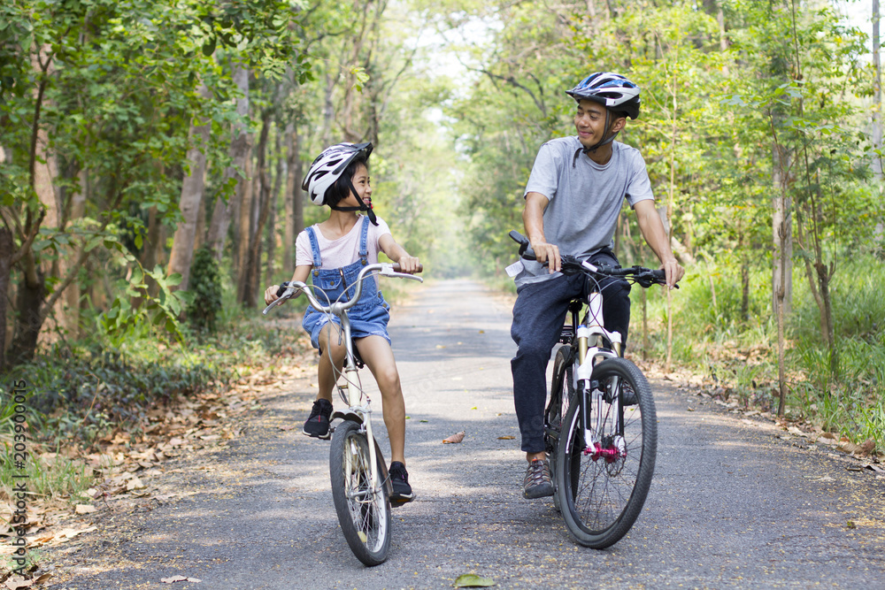 Wall mural happy father and daughter cycling in the park, togetherness relaxation concept