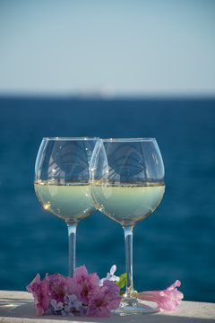 Two glasses with cold white wine served outside on terrace with pink tropical flowers, luxury resort with sea view, romantic vacation