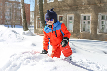 Fototapeta na wymiar 5 years little boy in warm ski suit playing outdoors in snow