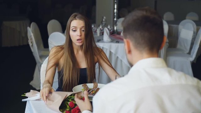 Angry young lady is arguing with her boyfriend while dining in restaurant then leaving. Lovers quarrel, negative emotions and relationship crisis concept.