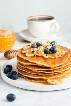 Stack of Pancakes With Banana Blueberry Walnuts and Honey. Tasty American Pancakes on white. Selective focus