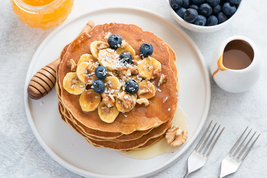 Pancakes with blueberries, banana, walnuts and honey on white plate. Stack of tasty pancakes with caramel syrup. Pancakes Breakfast with Honey