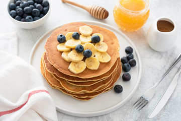 Pancakes stack with banana, blueberries and honey. Homemade american pancakes on white plate. Breakfast concept, horizontal composition