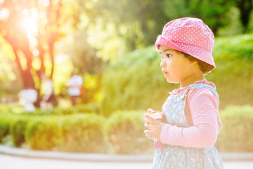 Side view portrait of cute elegant curly mixed race dark skinned toddler baby girl at summer park in sunset. Childhood and copying female psychology behavior concept. Copy space