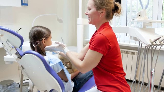 4k video of smiling female dentist giving teddy bear to girl patient before teeth examination