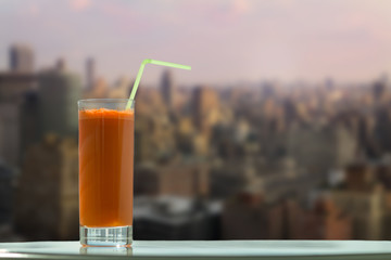 A glass of carrot juice with a straw in the cafe on the background Manhattan. New York City
