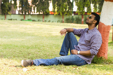 Young man wearing sunglasses relaxing and leaning against tree © RealityImages