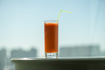 A glass of carrot juice with a straw in the cafe through the window on the background city