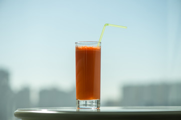 A glass of carrot juice with a straw in the cafe through the window on the background city