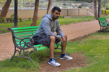 Obraz premium Young sportsman sitting on a wooden bench in a park