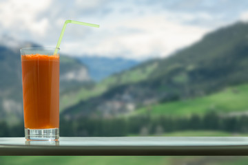 A glass of carrot juice with a straw in the cafe on the background of the Swiss Alps