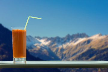 A glass of carrot juice with a straw in the cafe on the background of the Swiss Alps