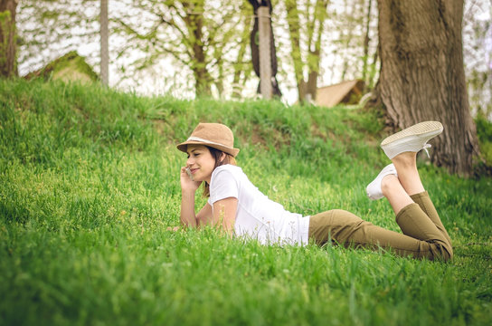 Young carefree woman talking on the phone in the nature, lying on the graas