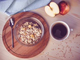 Breakfast. A bowl with muesli, a cup of coffee, the cut apple on a wooden table
