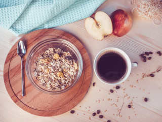 Breakfast. A bowl with muesli, a cup of coffee, the cut apple on a wooden table