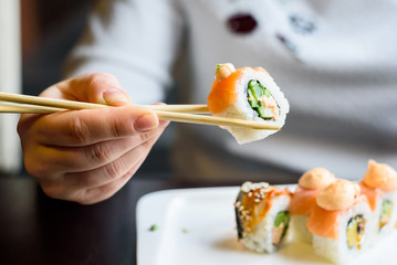 Young woman eats sushi rolls with chopsticks