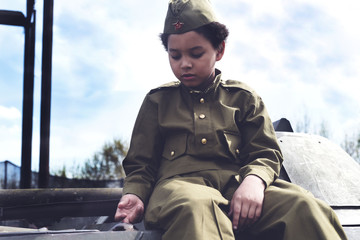Boy in the military uniform on the tank of time of Second World War. Kids in uniform. Soldier boy....