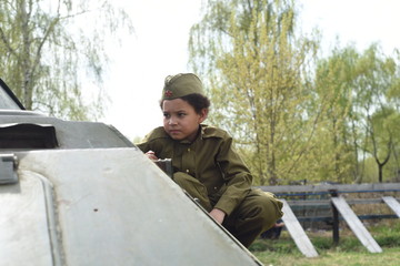 Fototapeta premium Boy in the military uniform on the tank of time of Second World War. Kids in uniform. Soldier boy. War time.