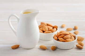 Almond oil and almonds on a white wooden background, selective focus