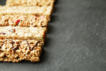 Row of mixed gluten free granola cereal energy bar with dried fruit & various nuts, gray concrete background. Healthy vegan super food, fitness dieting snack for sporty lifestyle. Top view, copy space
