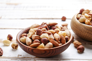 Mixed nuts in wooden bowl and scattered on table. Trail mix of pecan, almond, macadamia & brazil edible nuts with walnut hazelnut on wood textured surface. Background, copy space, top view, close up.