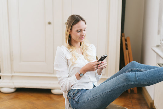 Smiling woman relaxing on chair with smartphone