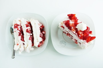 Two slices of Pavlova cake with strawberries and cream on white plates and background
