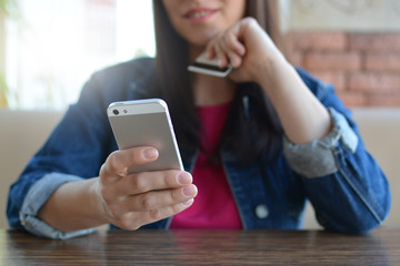 A brunette girl in a denim jacket is eating lunch in a cafe and using her phone. Communication through messenger. Casual loose clothing.