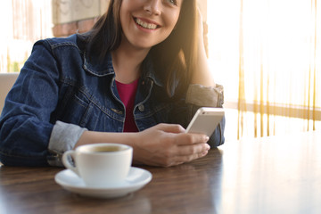 A brunette girl in a denim jacket is eating lunch in a cafe and using her phone. Communication through messenger. Casual loose clothing.