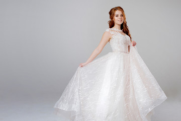Fototapeta na wymiar Lovely young woman bride in lavish wedding dress. Light background.