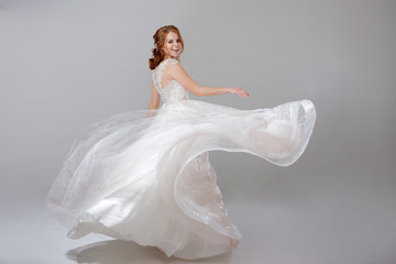 Fototapeta na wymiar Young woman spinning in a curvy wedding dress. woman bride in lavish wedding dress. Light background.