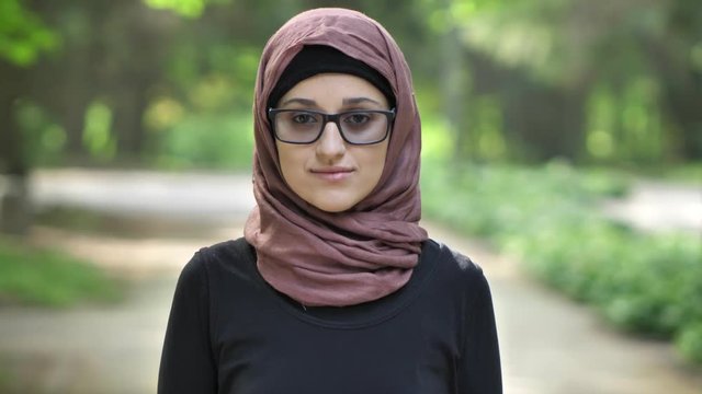 Portrait of a young girl in glasses wearing hijab, outdoor, in a park in the background. 50 fps