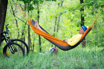 Tired man relaxes and meditates in a hammock after biking