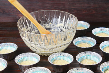 Dough in molds for muffins on a wooden table.