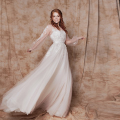 Fototapeta na wymiar Beautiful and romantic bride in wedding dress with long sleeves. Young redheaded woman in wedding dress