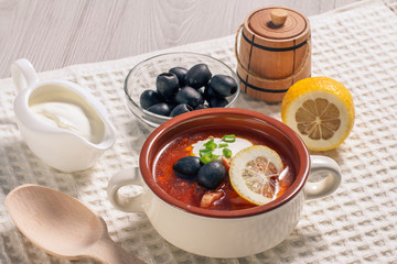 Soup saltwort with meat, potatoes, tomatoes, lemon, black olives and sour cream in ceramic soup bowl