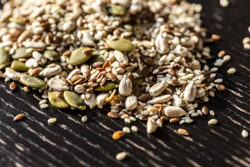 Mixed dry seeds pumpkin, sesame, sunflower, flax for healthy eating on the wooden black table.
