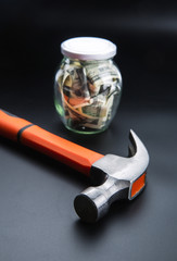 Hammer against jar full of dollars, money saving