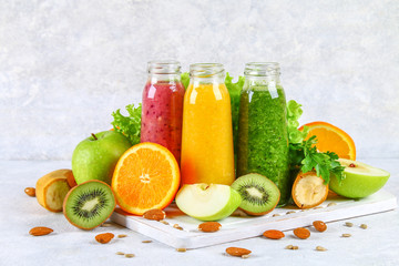 Green, yellow, purple smoothies in currant bottles, parsley, apple, kiwi, orange on a gray table.