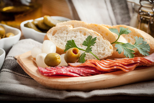 Tapas with sliced sausage, salami, olives, marinated onions, cucumber and parsley on a wooden table.