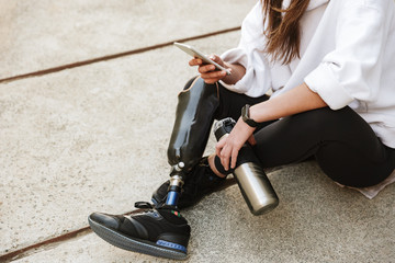 Cropped photo of handicapped woman in streetwear having bionic leg, sitting on concrete floor...