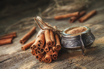 Ground cinnamon, cinnamon sticks, tied with jute rope on old wooden background in rustic style