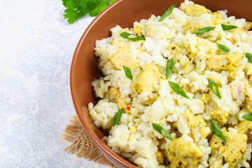 White steamed rice with slices of fried chicken fillet in a bowl on a concrete table.