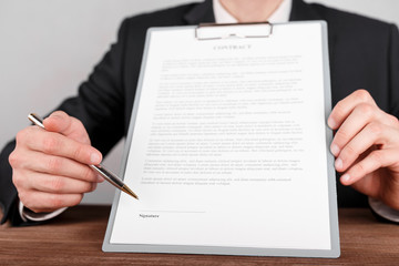 Businessman indicates the place for signing in the contract,which is attached to a clipboard.